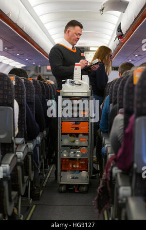 L'équipage de cabine de l'air / steward sert des boissons et des collations aux passagers - et prend - d'un paiement panier chariot pendant un vol Easyjet Banque D'Images
