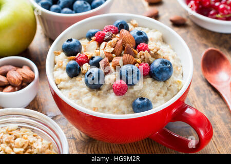 Gruau d'avoine chargé avec des bleuets, framboises, amandes et granola sur rouge tasse bol. Un petit-déjeuner sain, alimentation nourriture Banque D'Images