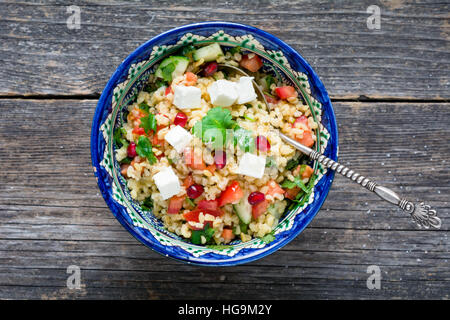 Taboulé salade avec du fromage blanc et de graines de grenade dans un bol sur fond de bois Banque D'Images