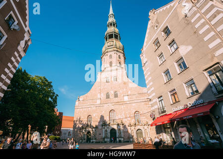 Riga, Lettonie - 1 juillet 2016 : Vue de dessous de l'église Saint Pierre, façade principale avec une flèche pleine hauteur entre deux immeubles anciens, fond bleu ciel clair Banque D'Images