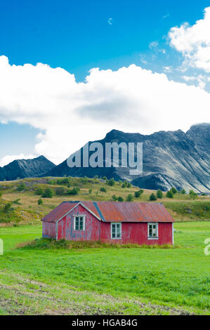 Petite maison en bois rouge abandonné dans la campagne avec des champs verts et les montagnes en arrière-plan Banque D'Images