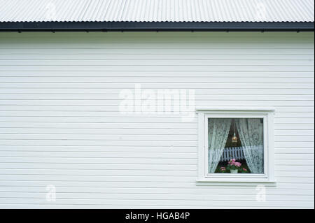 Vue latérale d'une maison en bois blanc avec petite fenêtre avec des rideaux et des fleurs Banque D'Images
