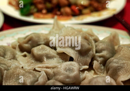 Chinois cuits boulettes en plaque sur table avec Gong Bao plat de poulet. Raviolis chinois sont traditionnellement servi pour le Nouvel An chinois, ou comme le Banque D'Images