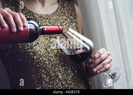 Close up of Caucasian horizontale femme retro vintage robe paillette d'or à verser le vin rouge dans un grand verre dans un bar Banque D'Images