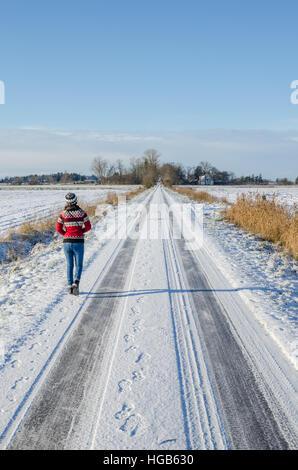 Young woman wearing red cavalier norvégien passe pour un hiver à pied avec un chien sur la route couverte de neige sur une belle journée ensoleillée Banque D'Images