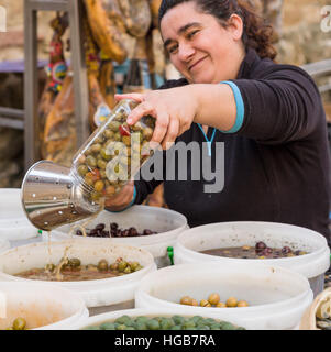 Vidange de l'olivier dans le marché. Un marché vendeur draine le vinaigre d'un bocal vert vient de charger des olives marinées pour les vendre à un client. Banque D'Images