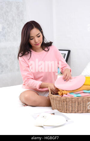 Pretty girl sitting on bed et flod ses vêtements dans la chambre. Banque D'Images