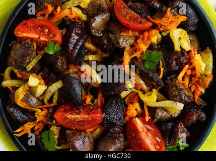 Morceaux de canard rôti, goose (viande, foie, cœur) avec des légumes (oignon, carotte, tomate) sur une poêle en fonte Banque D'Images