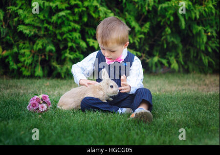 Petit garçon assis sur l'herbe avec lapin dans le parc d'été Banque D'Images