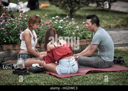 Groupe mixte d'amis s'assit sur l'herbe au parc local. Banque D'Images