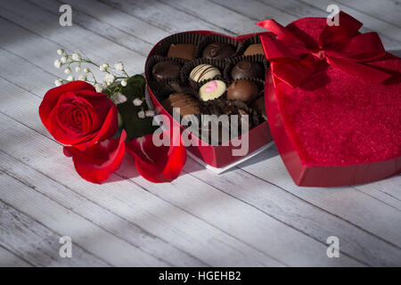 A ouvert une boîte en forme de coeur de bonbons au chocolat sur un fond de bois blanc avec une rose rouge Banque D'Images