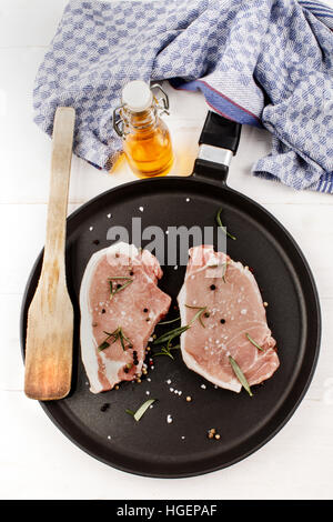 Côtelettes de porc cru prêt à fry sur une casserole avec le romarin, poivre et gros sel Banque D'Images