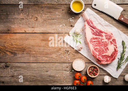 Matières tomahawk Pavé de boeuf avec des ingrédients à la cuisson : assaisonnement, du romarin frais et d'huile d'olive sur fond de bois, vue du dessus Banque D'Images