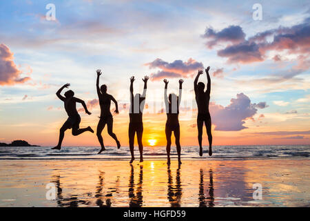 Groupe de personnes sautant sur la plage au coucher du soleil, les silhouettes des amis heureux en vacances Banque D'Images