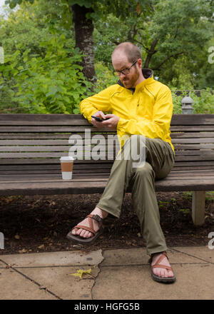 Homme assis sur un banc regarde l'appareil photo après regardant son téléphone Banque D'Images