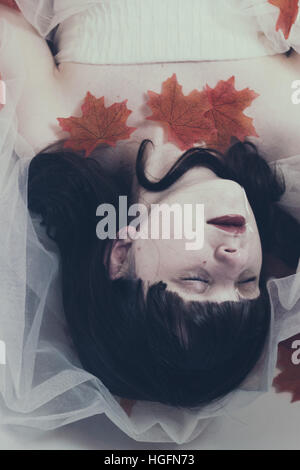Jeune femme brune couchée sur l'eau avec une robe blanche et feuilles d'érable rouge Banque D'Images