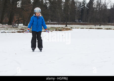 Adorable petite fille enfant patinage sur glace en hiver sous la neige à l'extérieur dans le parc sur étang gelé. Le port de casque de sécurité Banque D'Images