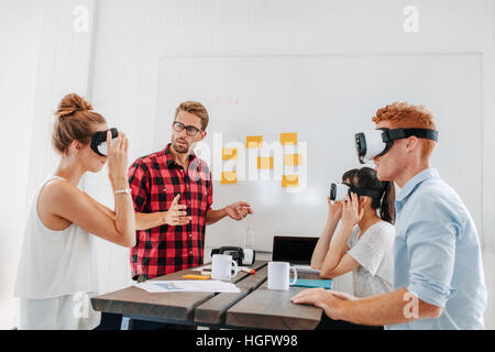 Les jeunes, hommes et femmes, assis à une table avec des lunettes de réalité virtuelle. Les essais de l'équipe Entreprises casque de réalité virtuelle en réunion de bureau. Banque D'Images