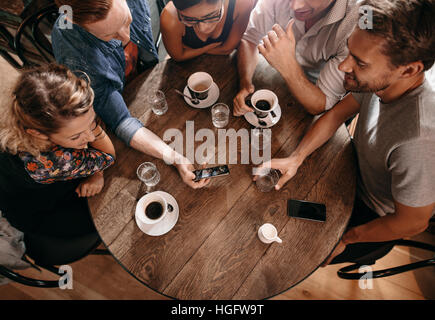 Groupe d'amis au café et à la recherche de téléphone intelligent. Homme montrant quelque chose à ses amis par séance. Banque D'Images