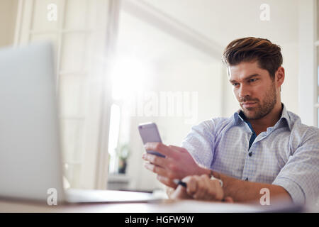Coup de jeune décontracté man sitting at desk using mobile phone. Handsome young man reading text message sur son téléphone intelligent. Banque D'Images