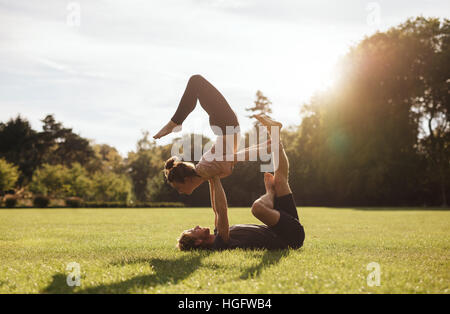 Monter couple doing yoga acrobatique exercice dans parc. Homme étendu sur l'herbe et l'équilibrage woman outdoors. Banque D'Images