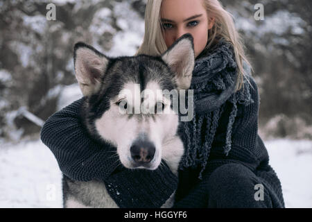 Portrait de fille avec gros chien malamute sur fond d'hiver. Fille est assise à côté de chien et hugging dog's neck. Banque D'Images