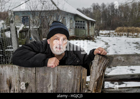 Portrait plein air de vieil homme ukrainien avec Visage en larmes qui se tenait à sa clôture près de négligé chambre en milieu rural village ukrainien Banque D'Images