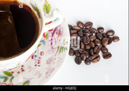 Une tasse et soucoupe remplie de café avec les grains de café sur fond blanc avec l'exemplaire de l'espace. Banque D'Images