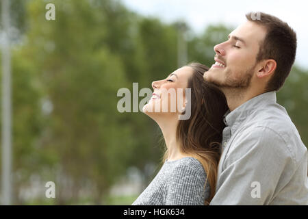 Vue de côté portrait d'un couple heureux, respirant l'air frais dans un parc avec des arbres verts dans l'arrière-plan Banque D'Images