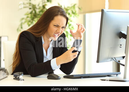 Furious businesswoman working on-line en utilisant un téléphone intelligent dans un bureau à l'office de tourisme Banque D'Images