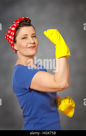 Femme de ménage heureux avec foulard, gants de nettoyage jaune et tissu, montrant ses muscles, indiquant le service de nettoyage puissant Banque D'Images
