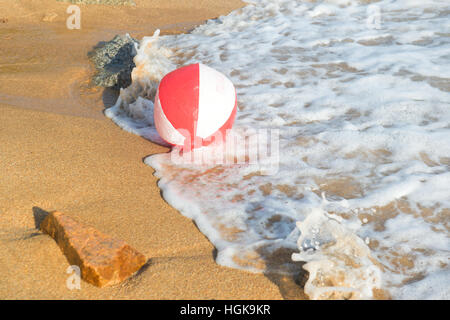 Ballon de plage rouge et blanc jouant avec les vagues et la mer à la plage Banque D'Images