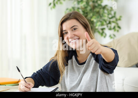 Happy student looking at you with Thumbs up assis sur le plancher de la salle de séjour à la maison Banque D'Images