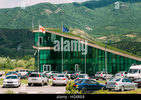 Mtskheta (Géorgie) - 20 mai 2016 : Le bâtiment en verre vert contemporain du poste de police avec un parking gratuit, le vert des montagnes en été fond Sunn Banque D'Images