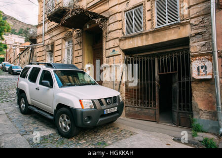 Tbilissi, Géorgie - 20 mai 2016 : l'avis de garé la voiture SUV Nissan Xterra blanc près de l'ancien bâtiment de la rue pavées étroites en été au crépuscule. Banque D'Images