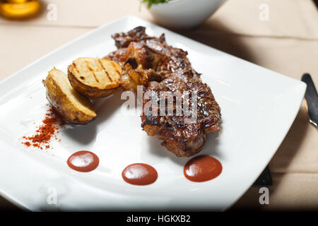 Steak avec pommes de terre grillées avec salade côté sur une plaque blanche Banque D'Images