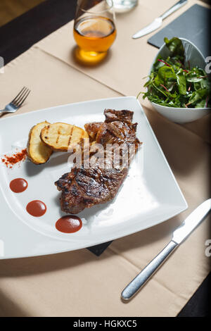 Steak avec pommes de terre grillées avec salade côté sur une plaque blanche Banque D'Images