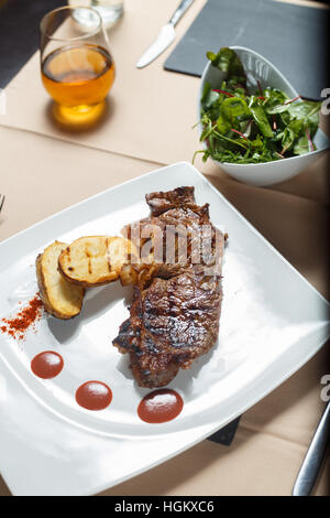 Steak avec pommes de terre grillées avec salade côté sur une plaque blanche Banque D'Images