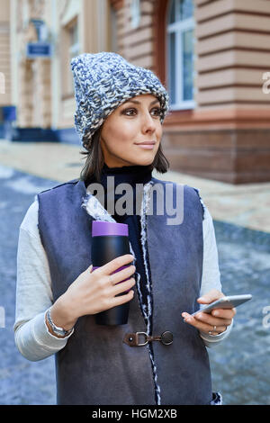 La jeune fille avec un smartphone et Thermocup Banque D'Images