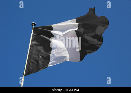 Rayé noir et blanc d'un drapeau qui flotte dans la brise d'une rapide contre un ciel bleu. Banque D'Images