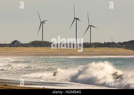 Les éoliennes d'un parc éolien se tenir le long d'une côte sablonneuse de Wexford en Irlande avec de puissantes vagues se brisant sur le rivage Banque D'Images