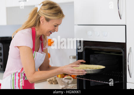 Jolie blonde woman putting tart dans le four pour la cuisson Banque D'Images