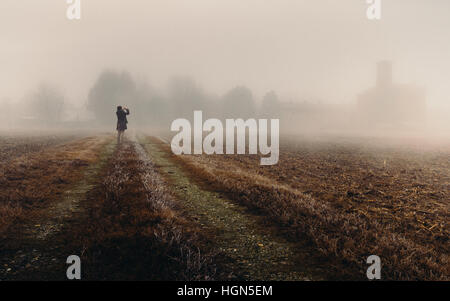 Femme dans la distance à la recherche dans une église de l'épais brouillard de la région Lombardie en Italie au cours de l'hiver, champ de maïs congelé Banque D'Images