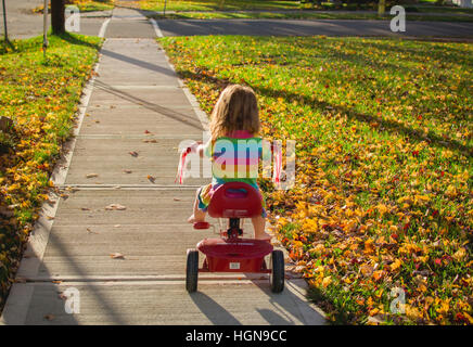 Une jeune fille monte un tricycle dans une petite ville des États-Unis. Banque D'Images