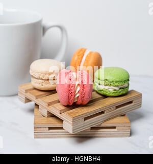 Macarons colorés et sucrés servis sur de petites palettes bois avec tasse de café sur une texture en arrière-plan. Dessert traditionnel français. Banque D'Images