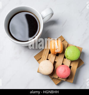 Macarons colorés et sucrés servis sur de petites palettes bois avec tasse de café sur une texture en arrière-plan. Dessert traditionnel français. Vue d'en haut. Banque D'Images