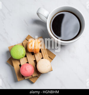 Macarons colorés et sucrés servis sur de petites palettes bois avec tasse de café sur une texture en arrière-plan. Dessert traditionnel français. Vue d'en haut. Banque D'Images