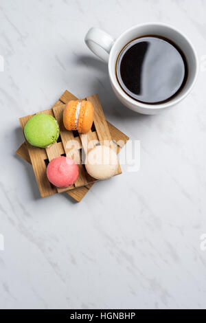 Macarons colorés et sucrés servis sur de petites palettes bois avec tasse de café sur une texture en arrière-plan. Dessert traditionnel français. Vue de dessus, copy space Banque D'Images