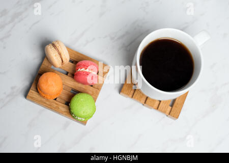 Macarons colorés et sucrés servis sur de petites palettes bois avec tasse de café sur une texture en arrière-plan. Dessert traditionnel français. Banque D'Images