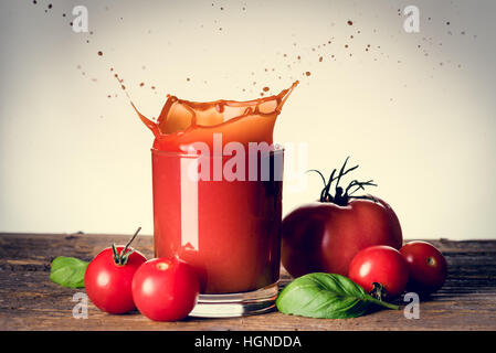 Éclaboussures de jus de tomates sur le verre sur la table en bois Banque D'Images